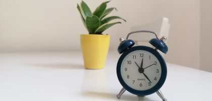 A blue vintage alarm clock and potted plant on a white surface, minimalistic decor.